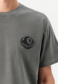Grå bomulds t-shirt med en rund "8" boldgrafik og tekst, der ligner "Santa Cruz", på venstre brystområde. Korte ærmer, standard pasform.