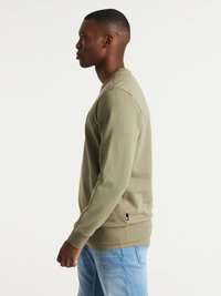 Sudadera verde oliva con puños y dobladillo de canalé. Corte casual con textura suave. Etiqueta visible en el lado inferior izquierdo.