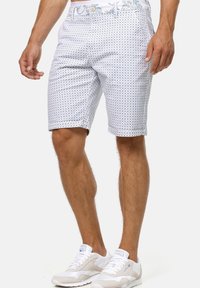 Shorts blancs avec un motif circulaire bleu et une taille décorative. Conçus en tissu léger, avec un bouton de fermeture et des poches.
