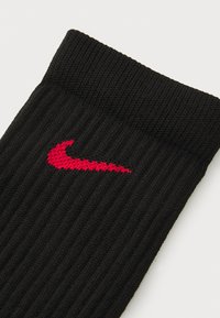 Calcetín negro acanalado hecho de tela de punto que presenta un prominente logo rojo de Nike. La parte superior tiene un diseño con puño para un ajuste seguro.