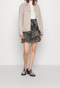 Ljust grå denimjacka över en vit topp, parat med en svart blommig volangkjol. Skinande silvriga loafers fulländar outfiten.