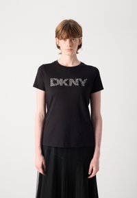 Črna bombažna majica s peterokrako "DKNY" logotipom iz rhinestones, okroglo izrezana in s kratkimi rokavi. Nosi se s prosojno črno krilom.