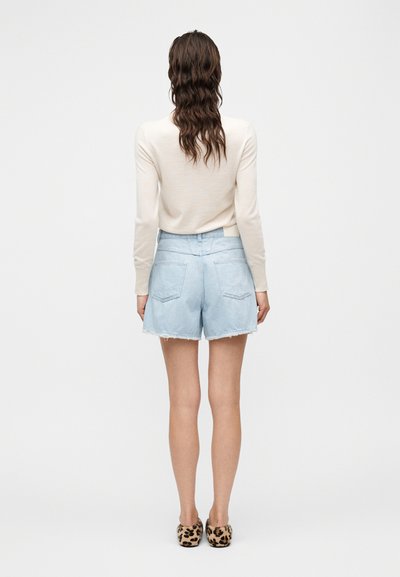 Ανοιχτό μπλε denim σορτς με ξεφτισμένο τελείωμα, δύο πίσω τσέπες, σε συνδυασμό με μια κρεμ μακρυμάνικη μπλούζα και παπούτσια με λεοπάρ μοτίβο.