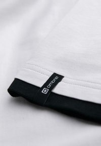 Bílá látka vrstvená přes černou látku s malou černou cedulkou označenou "ombre", která je přišitá blízko švu.