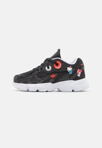 Zapatilla negra con materiales de malla y sintéticos. Presenta una suela blanca, ojales y adornos de personajes coloridos. Diseño distintivo y grueso.