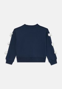 Felpa blu navy con scollo rotondo, polsini a costine e fiocchi bianchi decorativi sulle maniche. Tessuto morbido con vestibilità ampia.