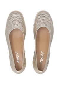 Béžové slip-on boty s текстurovaným svrškem obsahujícím geometrické výřezy, hladkým vnitřním podšíváním a plochou podrážkou s minimálními detaily.