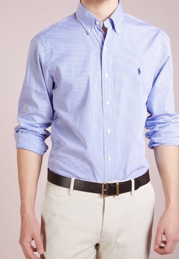 Homme portant une chemise à rayures bleu clair avec boutons et manches retroussées, pantalon beige et ceinture noire avec une boucle dorée.