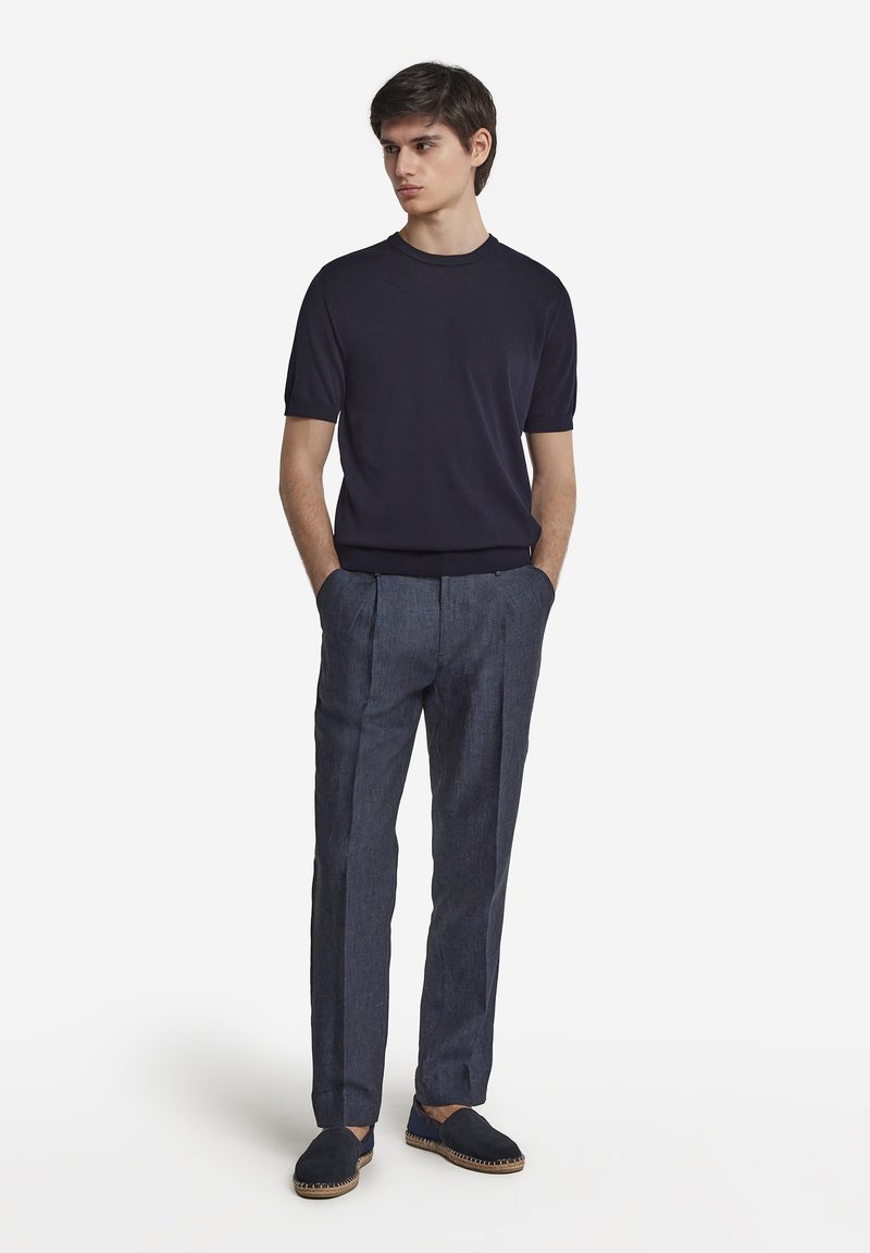 Marinblå kortärmad t-shirt i kombination med kolgrå skräddarsydda byxor och marinblå espadrillos. Slät tyg, strukturerad passform och minimalistisk design.