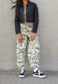 Kort svart jacka över en brun topp, i kombination med löst sittande, kamouflagemönstrade cargobyxor i grönt och beige, samt svarta sneakers.