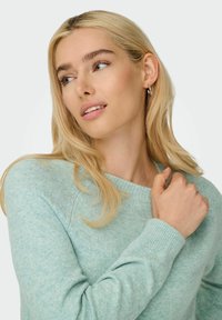 Light teal knitted sweater with a crew neckline and ribbed cuffs, featuring a soft texture and subtle heather pattern. Model gently touching shoulder.
