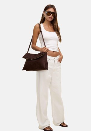Braune Wildleder-Handtasche mit flachem Design und Reißverschluss, kombiniert mit einem weißen Tanktop und weißen weiten Hosen. Dunkle Sonnenbrillen runden den Look ab.