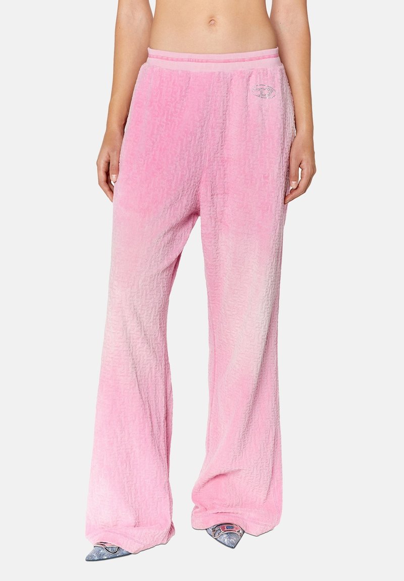 Femme portant un pantalon large à taille haute rose texturé avec un petit logo sur la cuisse, associé à des chaussures argentées à bout pointu.