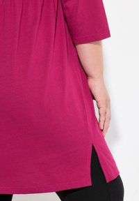 Túnica fucsia de manga corta, con aberturas laterales en el dobladillo para mayor movimiento. Fabricada con material suave y ligero.