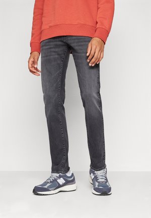 Jean slim gris foncé, en denim, avec un léger effet délavé et un design classique à cinq poches, associé à des baskets bleu marine.