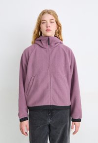 Chaqueta de forro polar en morado claro con cremallera delantera, capucha y bolsillos laterales. Presenta puños y dobladillo en negro para un contraste. Textura suave.