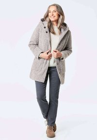 Hellgrauer, strukturierter Mantel mit Kapuze, großen Knöpfen, getragen über einem cremefarbenen Pullover, kombiniert mit dunklen Jeans und braunen Schnürschuhen.