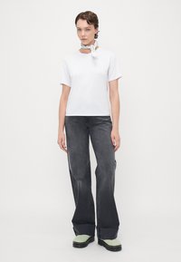 T-shirt bianco a maniche corte con scollatura a girocollo, abbinato a jeans larghi neri scoloriti e scarpe stringate con suola verde. Accento con una sciarpa semplice.