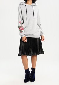 Felpa grigia con ricami floreali sulle maniche, abbinata a una gonna nera plissettata e stivaletti in velluto blu. Tessuto testurizzato e design casual.