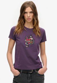 Camiseta de algodón morada con un colorido diseño bordado que incluye un corazón y elementos florales, de mangas cortas y con cuello redondo.