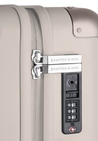 Hartschalenkoffer in hellem Beige mit glatter Textur, doppelten Metallreißverschlüssen, Zahlenschloss und "Kapten & Son" Logodetail.