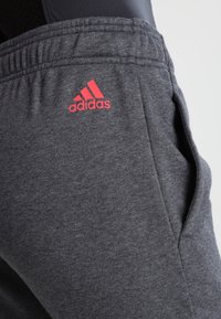 Grijze joggingsbroek van zacht materiaal, met een elastische tailleband en zakken. Het Adidas-logo is zichtbaar in felroze op de dij.