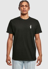 Sort bomuld t-shirt med et lille hvidt fredssymbol på venstre bryst. Klassisk rund hals, korte ærmer og afslappet pasform.