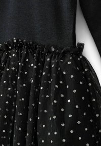 Czarny strój z dopasowaną górą i teksturowaną spódnicą z tiulu, ozdobioną srebrnymi groszkami i marszczoną talią.