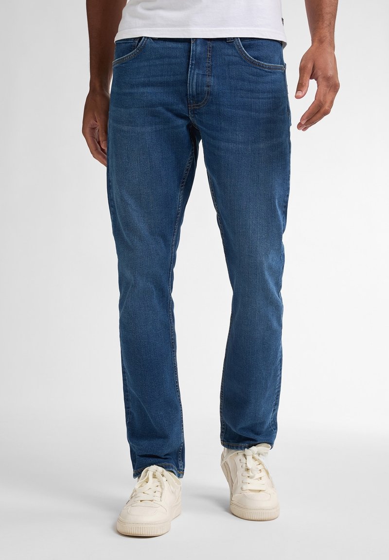 Jeans blu scuro in denim, caratterizzati da un taglio dritto classico, design a cinque tasche e una finitura leggermente testurizzata. Abbinati a sneakers bianche.