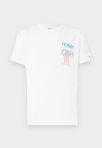 T-shirt en coton blanc avec un texte "TOMMY" en bleu et un graphique d'un personnage avec un motif drapeau américain au niveau de la poche poitrine.