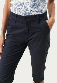 Pantalons cropped en mélange de coton bleu marine avec une texture lisse, présentant des poches avant et une coupe décontractée. Taille avec passants de ceinture.