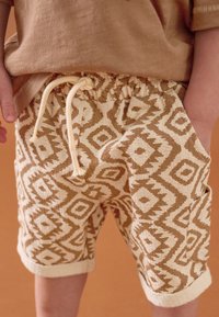 Shorts à motifs en beige clair et crème avec un motif en losange, taille élastique avec cordon de serrage, et ourlets retroussés ; tissu texturé.