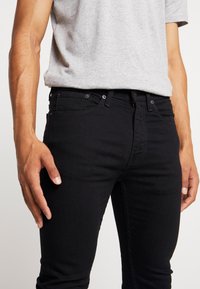 Μαύρο τζιν παντελόνι με εφαρμογή slim, κλασικό σχέδιο πέντε τσεπών και φερμουάρ με κουμπί. Το υλικό είναι μαλακό με ελάχιστη φθορά.