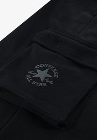 Μαύρο βαμβακερό παντελόνι φόρμας με μπροστινή τσέπη, σχεδιασμό λογότυπου "Converse All Star" σε γκρι χρώμα και αστέρι, λεία υφή και απλή στυλιστική προσέγγιση.
