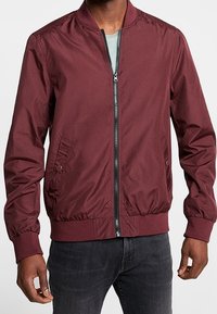 Bordowa kurtka bomberka z zamkiem z przodu, ściągaczami przy mankietach, bocznymi kieszeniami oraz gładkim, lekkim materiałem. Posiada klasyczny design kołnierza.