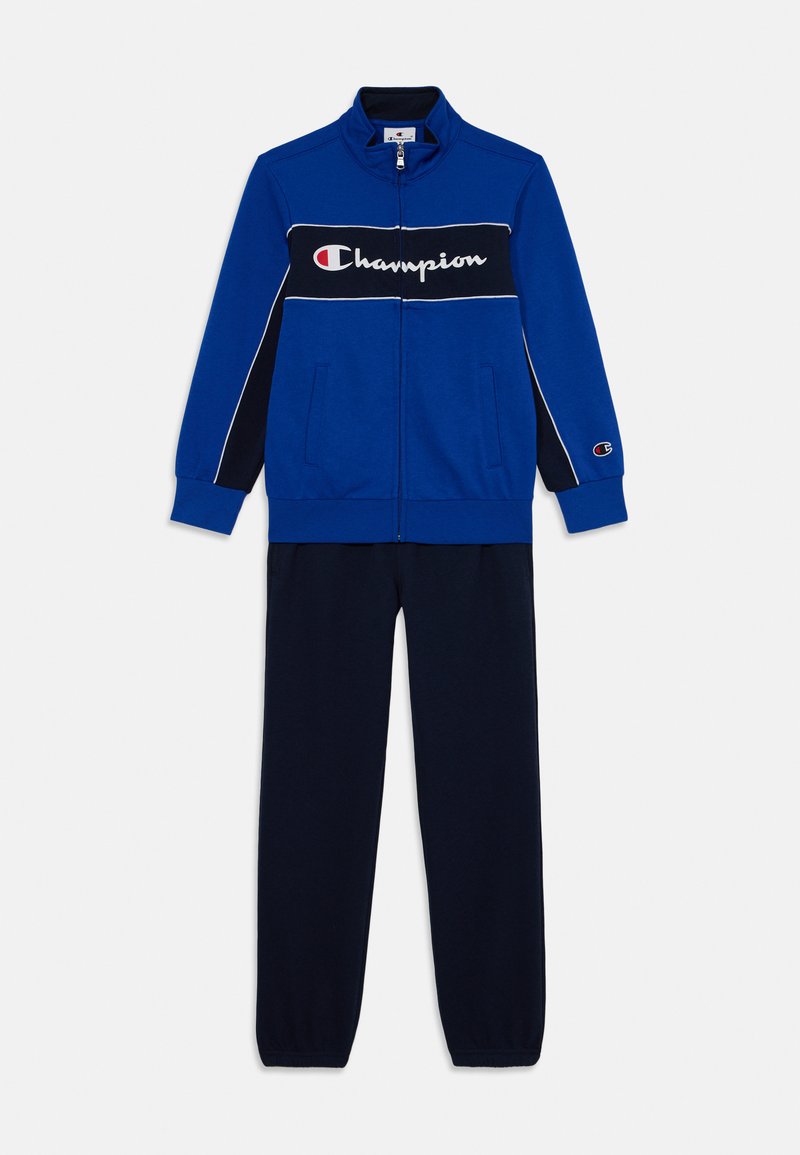 Modrá zipová tréningová bunda s čiernym a bielym pruhom, logo "Champion" v bielej farbe na hrudi, spárovaná s námorníckymi teplákmi. Bavlnený materiál.