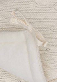 Couverture en tricot blanche avec un dessous doux et pelucheux, ornée d'un accent de nœud en ruban beige clair. Surface texturée avec de petits motifs.