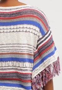 Poncho lavorato a maglia multicolore con strisce blu, rosse, beige e bianche; presenta un motivo a rete aperta e frange lungo l'orlo.