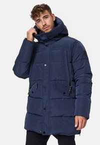 Doudoune bleu marine avec col haut, fermeture à boutons, motif matelassé horizontal et deux poches avant. Tissu doux et isolant.