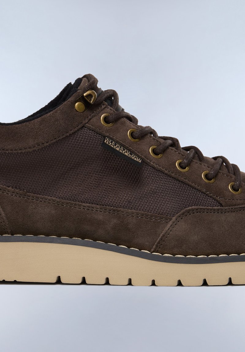 Scarpa in suede marrone e mesh con occhielli dorati, suola beige, motivi testurizzati e un'etichetta con logo sul lato. Presenta un design low-top.