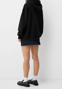 Černá oversized mikina s kapucí, doplněná o džínsovou minisukni. Oblečení doplňují černé boty a bílé ponožky.