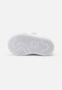 White sneaker sole with a textured, honeycomb pattern. Features a slight curve and embossed brand logo in the center. Durable rubber material.