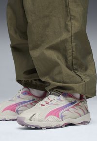 Des baskets avec une tige en maille beige, ornées d'accents roses et violets. La semelle est blanche avec une base translucide lavande.