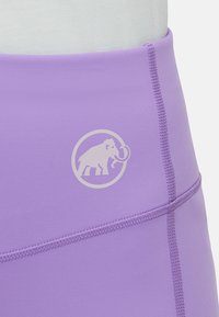 Lavendel träningstights i slät tyg, med en cirkulär vit logotyp av ett mammut; inkluderar flatlock-sömmar för komfort.