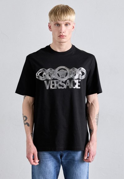 Tricou din bumbac negru, cu un logo Versace argintiu proeminent și un design cu lanț pe față. Mâneci scurte și croială lejeră.