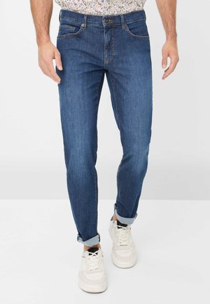 Dark blue denim jeans featuring a straight leg design, light stitching details, and rolled cuffs. Paired with white sneakers.