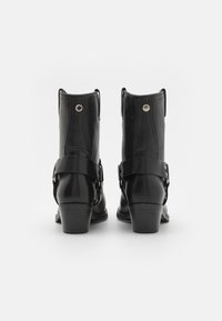 Botines de cuero negro con punta redondeada, tacón corto en bloque, correas laterales con hebillas y detalles metálicos en la parte trasera.
