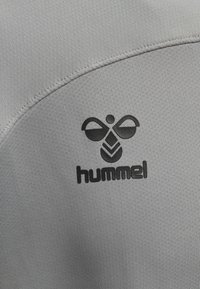 Tessuto sportivo grigio con il logo Hummel nero, con un'ape stilizzata e un design a triangolo. Texture liscia, dettagli cuciti sui bordi.