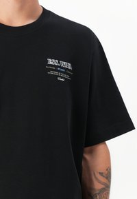 Sort t-shirt med korte ærmer, der har et hvidt trykt logo på brystet. Lavet af blødt stof med en afslappet pasform, velegnet til hverdagstøj.