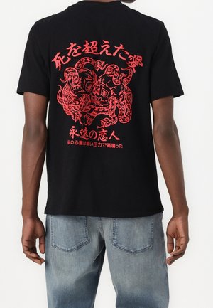 Czarny bawełniany t-shirt z czerwonym wzorem graficznym, zawierającym stylizowany tekst i ilustrację stworzenia na plecach. Krótkie rękawy, luźny krój.